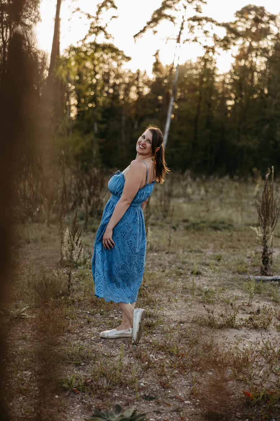 Nina Herzog im blauen Sommerkleid, lachend über die Schulter blickend, im warmen Abendlicht